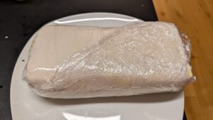 Rouleau de bœuf bien serré dans du film alimentaire, au frais sur une assiette