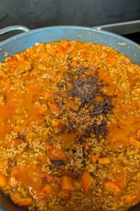 Poêle de bœuf haché et de sauce tomate orangée avec des morceaux de poivron rouge et un tas de chocolat noir finement haché au centre, avant d'être mélangé