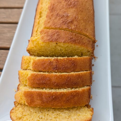 Pain de maïs doré sans gluten, avec quatre tranches alignées sur un long plat blanc, croûte dorée et mie jaune un peu friable