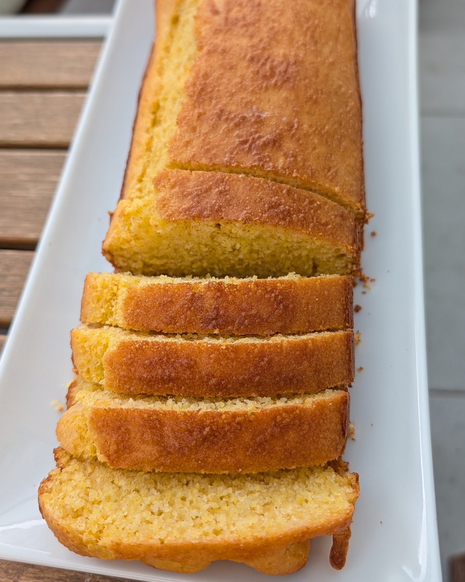 Pain de maïs doré sans gluten, avec quatre tranches alignées sur un long plat blanc, croûte dorée et mie jaune un peu friable