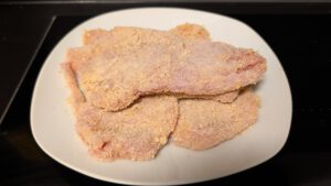 Escalopes crues panées dans une chapelure orange pâle, empilées sur une assiette blanche avant la cuisson