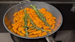 Bâtonnets de carotte et brins de romarin frais dans une large poêle avant la cuisson
