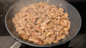 Morceaux de porc cuits dans une poêle grise, avec de la vapeur qui s'en échappe