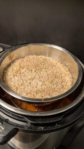Instant Pot avec un bol en inox rempli de grains de sarrasin cuits posé sur un trépied dans la cuve après la cuisson sous pression ; les boulettes et la sauce en dessous sont à peine visibles