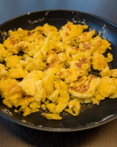 Morceaux dorés de Kaiserschmarrn déchiré dans une poêle antiadhésive sombre, sur une table en bois foncé