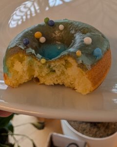 Mini donut glacé avec des vermicelles, croqué, montrant la mie jaune et tendre, sur une assiette blanche