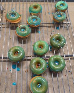 Mini donuts glacés en vert et bleu, avec des vermicelles colorés, sur une grille de refroidissement posée sur du papier sulfurisé