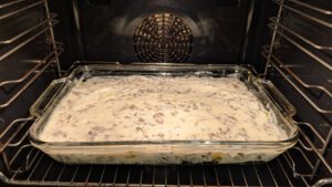 Moussaka avant cuisson dans un plat rectangulaire en verre au four, recouverte d'une sauce crémeuse pâle où des miettes de viande hachée apparaissent