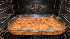 Moussaka cuite dans un plat rectangulaire en verre au four, dessus doré moucheté de brun et couches visibles sur le côté du plat