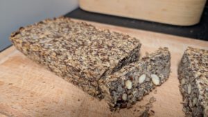 Pain aux graines cuit à dessus plat avec une tranche coupée, amandes entières et graines visibles dans la mie dense