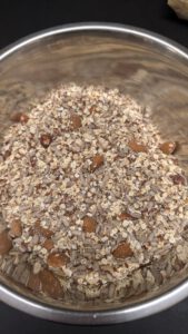 Mélange sec de flocons d'avoine, de graines de tournesol, de graines de lin et de fruits à coque entiers dans un saladier en inox, avant l'ajout du liquide