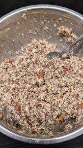 Pâte épaisse à pain aux graines avec une cuillère dans un saladier en inox, flocons d'avoine, graines, morceaux de fruits à coque et graines de chia grises visibles