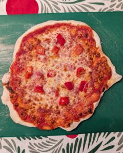 Pizza sans gluten tout juste sortie du four, avec fromage doré, sauce tomate et dés de poivron rouge sur une planche verte farinée