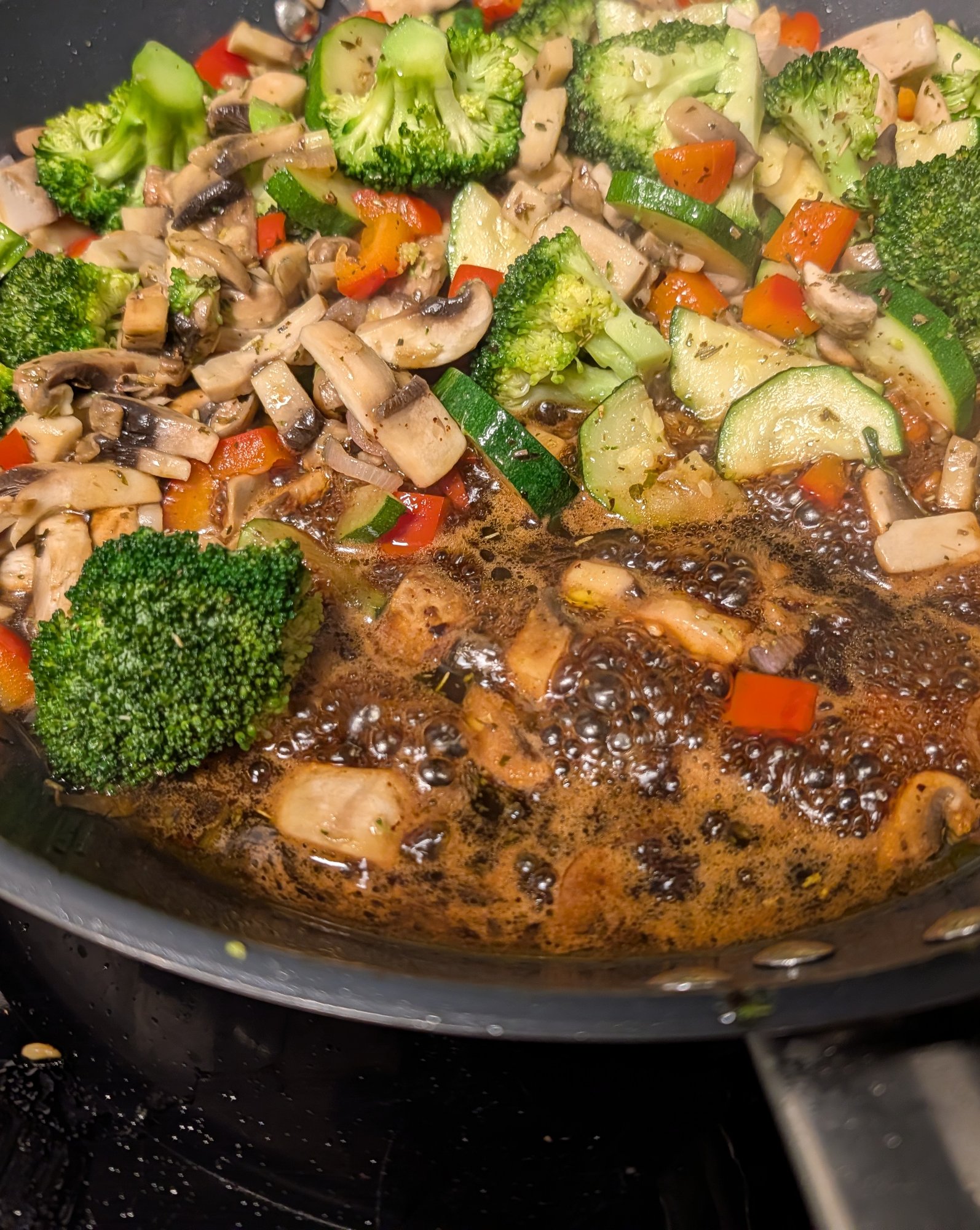 Poêle remplie de bouquets de brocoli, de lamelles de champignons, de rondelles de courgette et de morceaux de poivron rouge, avec un sirop balsamique sombre qui bouillonne au fond