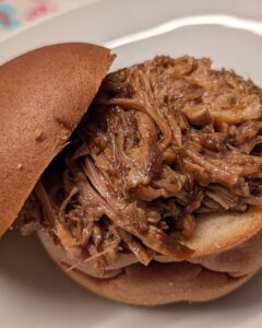 Gros plan d'un burger au pulled pork, la moitié supérieure du pain posée de biais, sur une assiette blanche