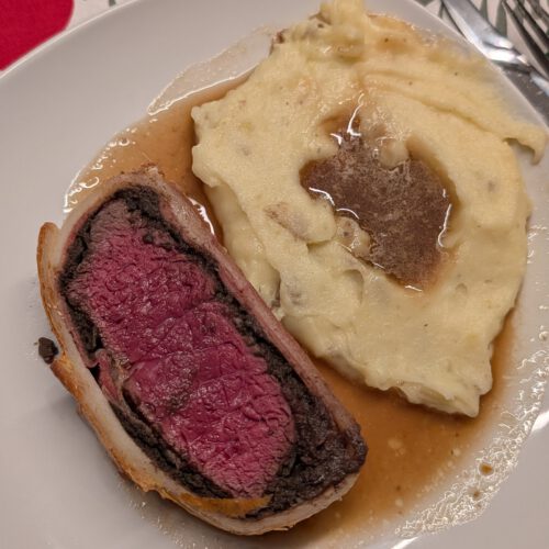 Purée de pommes de terre crémeuse nappée de sauce brune, dans une assiette à côté d'une tranche de Beef Wellington