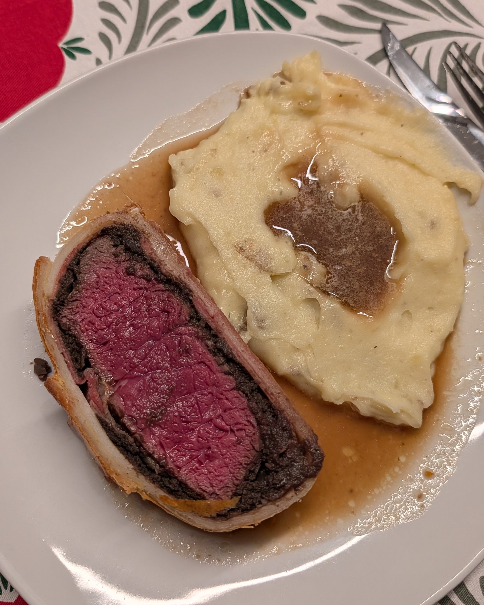 Purée de pommes de terre crémeuse nappée de sauce brune, dans une assiette à côté d'une tranche de Beef Wellington
