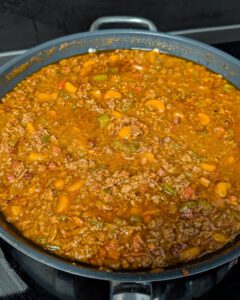 Ragù bolognaise qui mijote dans une sauteuse large, avec du bœuf haché, de la pancetta, de la carotte et du céleri