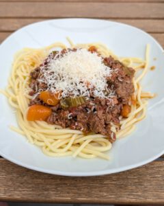 Assiette de spaghettis nappés de ragù bolognaise et d'un petit tas de fromage râpé, posée sur une table en bois