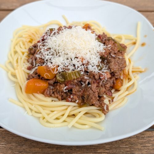 Assiette de spaghettis nappés de ragù bolognaise et d'un petit tas de fromage râpé, posée sur une table en bois