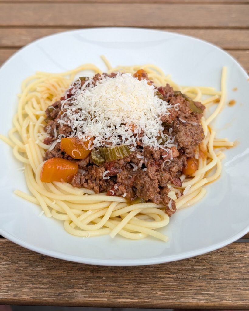 Assiette de spaghettis nappés de ragù bolognaise et d'un petit tas de fromage râpé, posée sur une table en bois