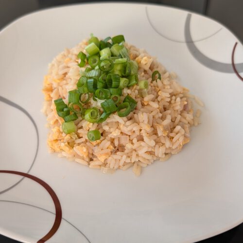 Riz sauté aux œufs brouillés, garni d'oignons nouveaux émincés, dans une assiette blanche à motifs gris et bruns